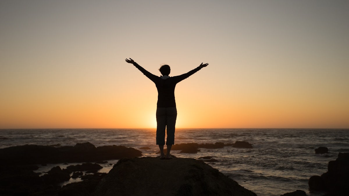 Silhouette of a person with arms raised at sunset.